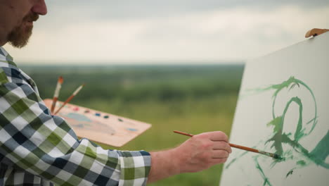 a dedicated artist, dressed in a checkered shirt. he holds a paint palette in one hand and a brush in the other as he gently applies green paint to a large white canvas