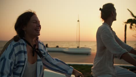 Close-up-shot-of-a-guy-in-light-clothes-and-a-girl-in-a-striped-shirt-riding-bicycles-along-the-beach-near-the-sea-at-dawn.-Active-lifestyle-morning-trip-to-the-sea