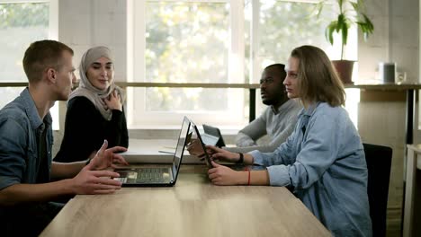 Group-Of-Four-Young-People-Sitting-At-The-Table-With-Open-Laptops-And-Have-Disscussion