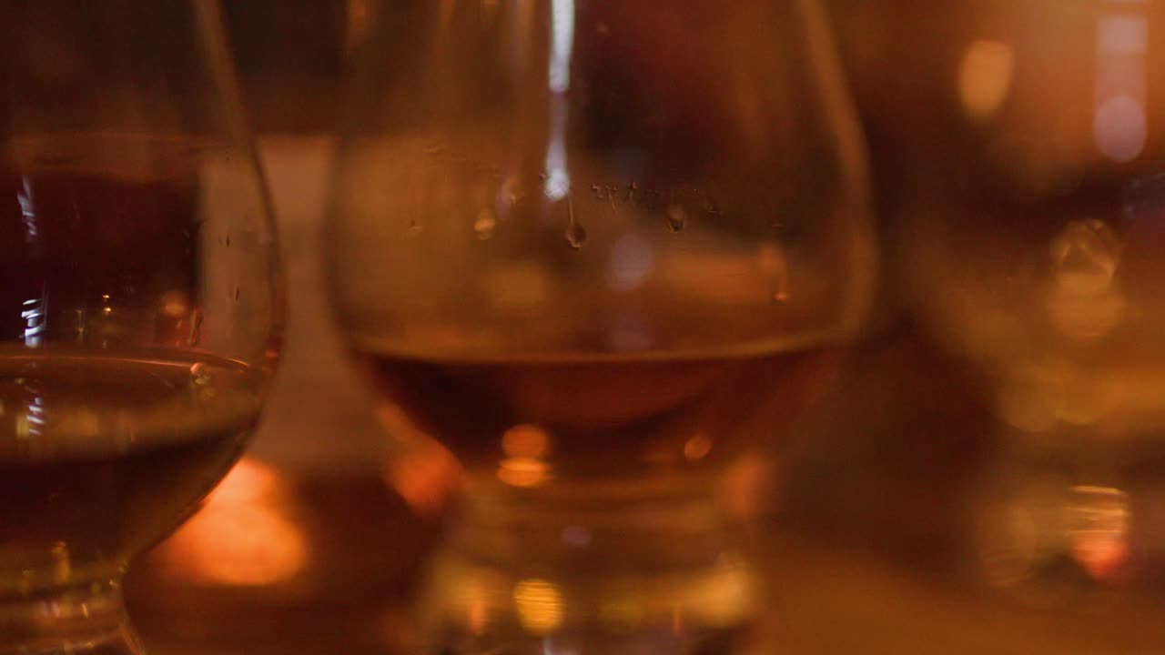 Una mano si muove su una fila di bicchieri di whisky ambrato sotto la calda luce di un pub