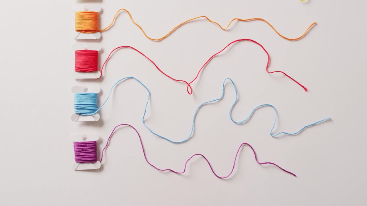 vídeo de seis bobinas de hilos de bordado de colores desenrollados sobre un fondo blanco