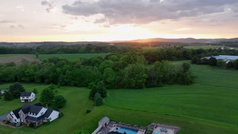 white farmhouse-style home with gabled roof and porch beside brick house with dormer windows and backyard gazebo and pool. aerial view. american suburb neighborhood of pa, united states at sunset.