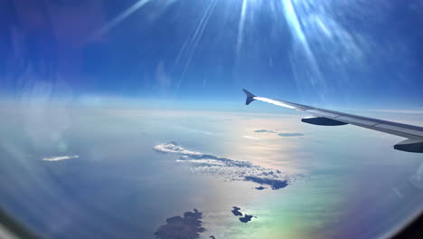 airplane wing view over crete, greece, with scattered islands and a bright sunny sky