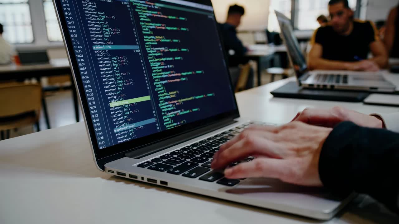 Close-up angle of hands typing code on a laptop in a collaborative workspace