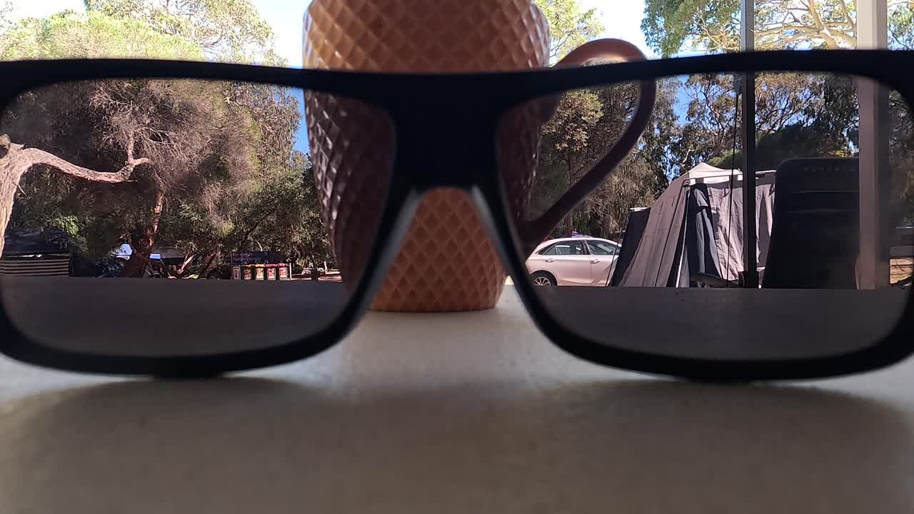 A pair of sunglasses frames a serene outdoor setting with a cup and tent in view