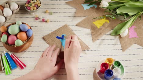 happy easter holiday. woman painting bunny on garland top view. preparing for easter, decorating room, colored eggs. christian celebration, family traditions.