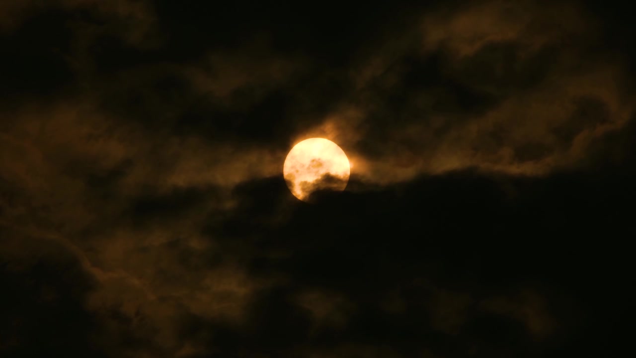 Medium shot, dark orange full moon glowing with black clouds moving across gently.