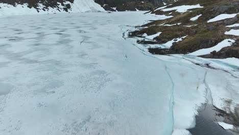 a partially frozen lake in norway with snow-covered shores and surrounding landscape, aerial view