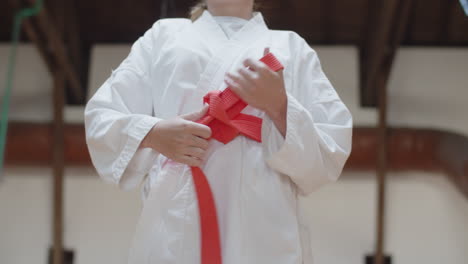 medium shot of girl tying orange belt on kimono in practice room