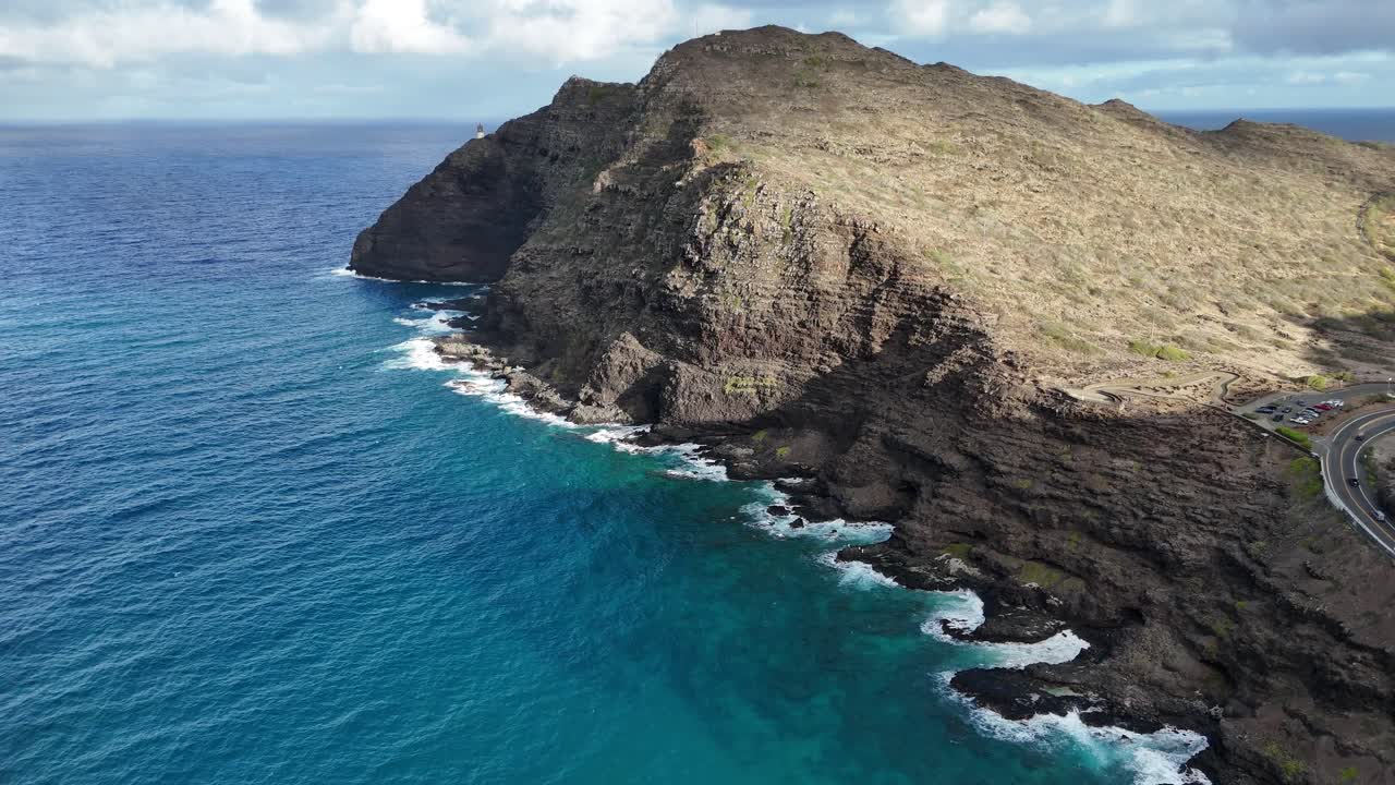 Drone aerial view of Oahu, Hawaii, featuring a rocky mountain into the blue ocean sea. Dramatic coastline, tropical island scenery, and vibrant ocean waters