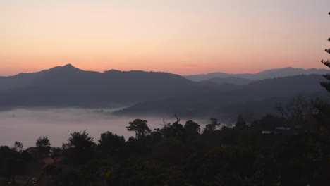 young asian woman enjoying sunrise from balcony in misty tropical forest of thailand