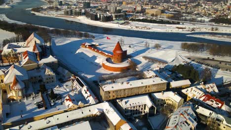 Drone-shot-of-the-historic-old-red-brick-Kaunas-Castle-in-Kaunas-old-town,-near-Neris-river,-in-Lithuania-during-cold-snowy-winter,-zooming-in