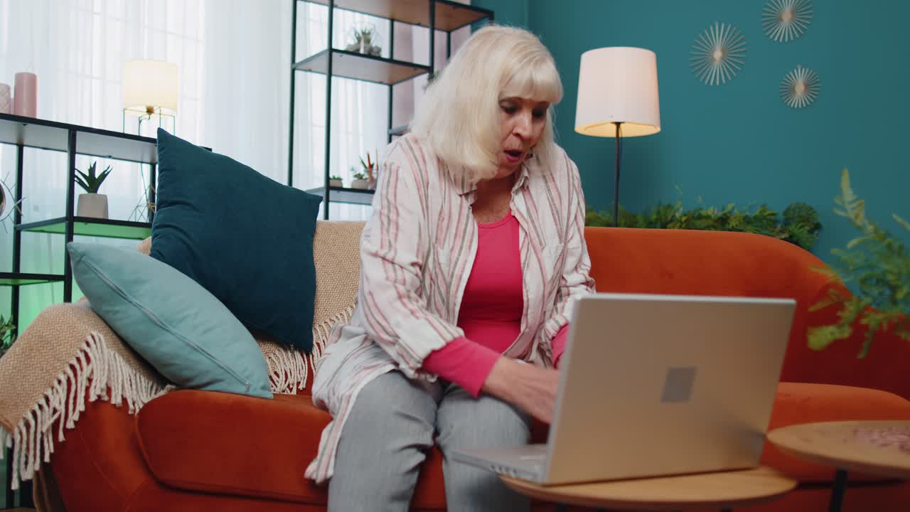 Satisfied cheerful senior grandmother freelancer woman pressing button on laptop and counting money