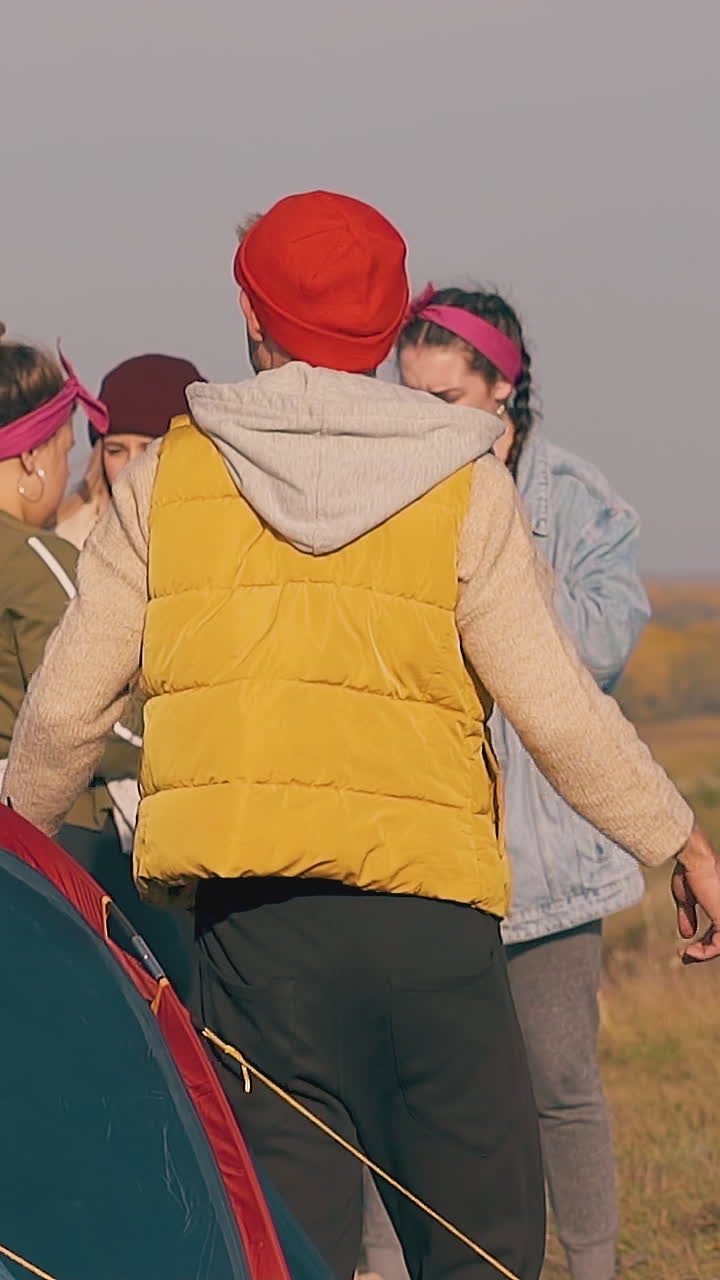 guy in orange warm vest gets out of tent ladies look at man standing at campfire lit by autumn sun in morning slow motion