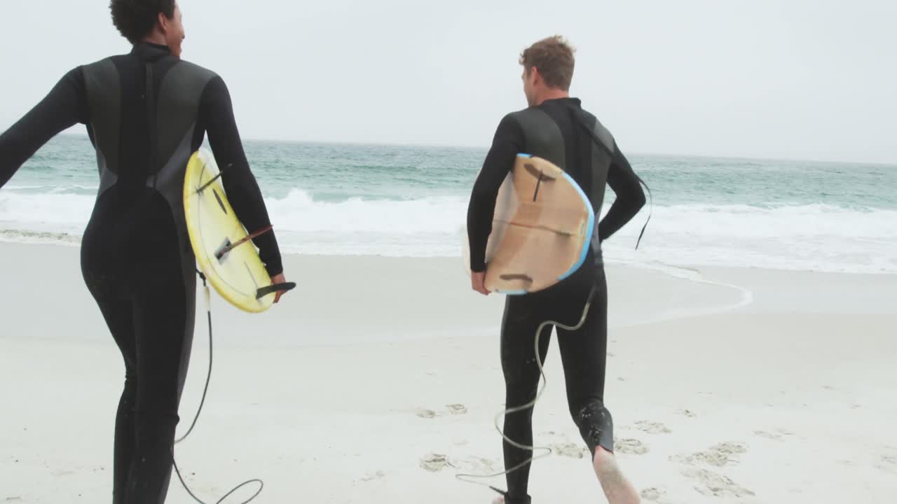 vista trasera de dos surfistas masculinos corriendo juntos con una tabla de surf en la playa 4k