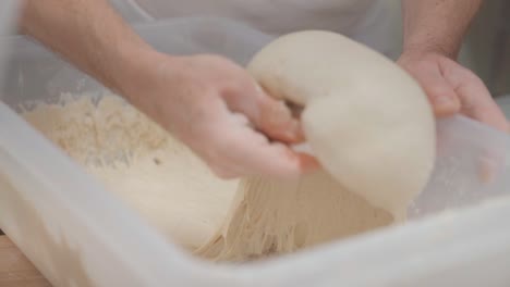 a baker takes a piece of yeast dough from a plastic container to make patties