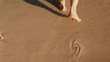 A-slow-motion-close-shot-following-a-woman´s-feet-walking-on-a-beach,-near-the-water-at-sunset