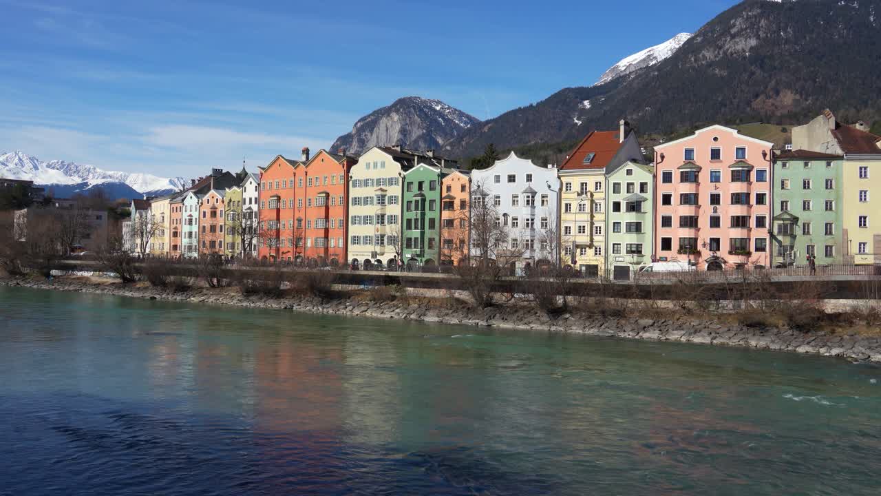 Traditionelle Innsbrucker Architektur am Inn unter klarem blauem Himmel und schneebedeckten Alpengipfeln.