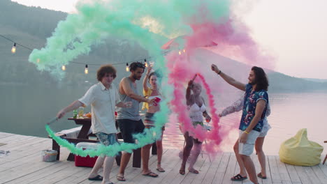 jóvenes bailando con bombas de humo de colores en el muelle del lago