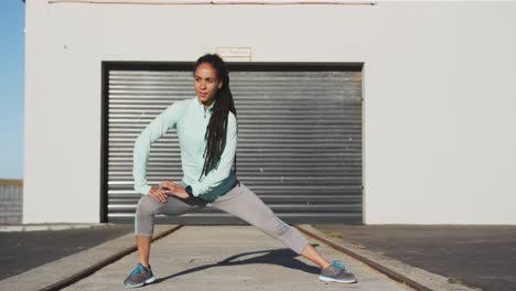 african american woman in sportswear stretching in street before exercising