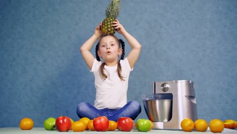 Funny kid playing with pineapple. Little girl is sitting on the table with many fresh fruits. New squeezer near organic food.
