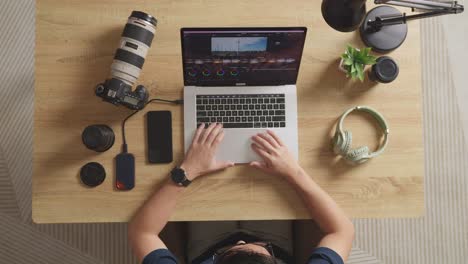 top view zoom in shot of a male color grading sitting in the workspace using a laptop next to the camera editing the video at home