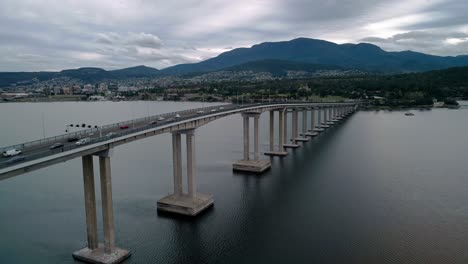 Forward-aerial-shot-of-a-bridge-in-Tasmania,-Australia-with-cityscape-at-background