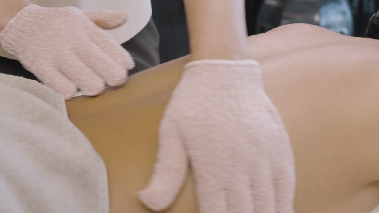 супер мягкая кожа красивой женской спины, витализирующий скраб для тела на спине в перчатках, восстанавливающая процедура для кожи в оздоровительном спа-центре, уход и лечение кожи, женщина наслаждается массажем в спа-центре