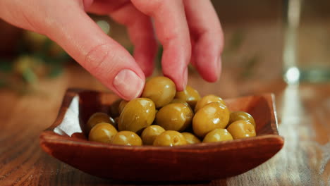 hand picking olives from a wooden bowl