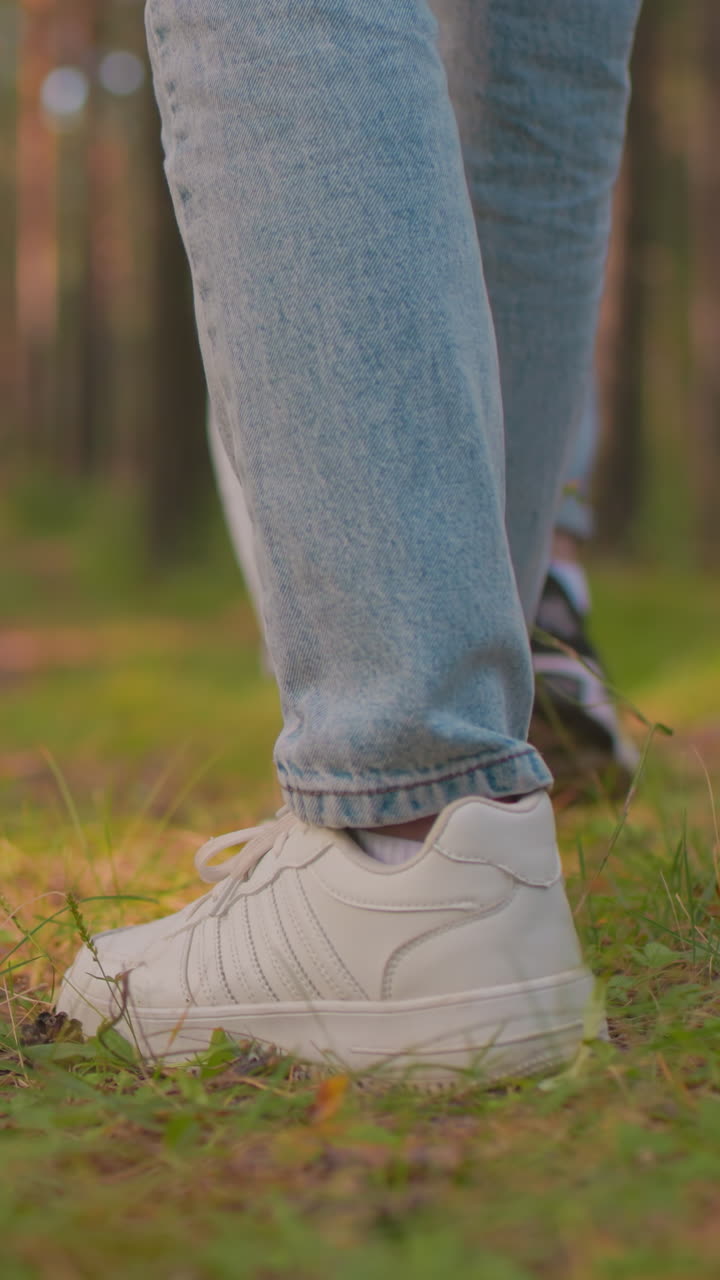 Close-up rear view of two hikers walking along forest trail, one wearing white sneakers, other in black sneakers, both dressed in blue jeans