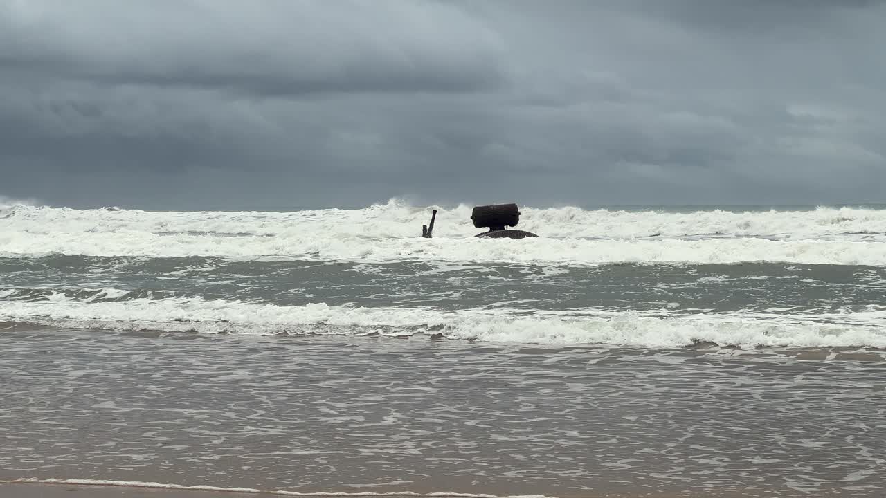 스페인 해안에서 파도가 해변에 부히고, 구름이 가득한 어두운 날씨를 배경으로 해양과 자연의 영원한 상호 작용을 묘사합니다.