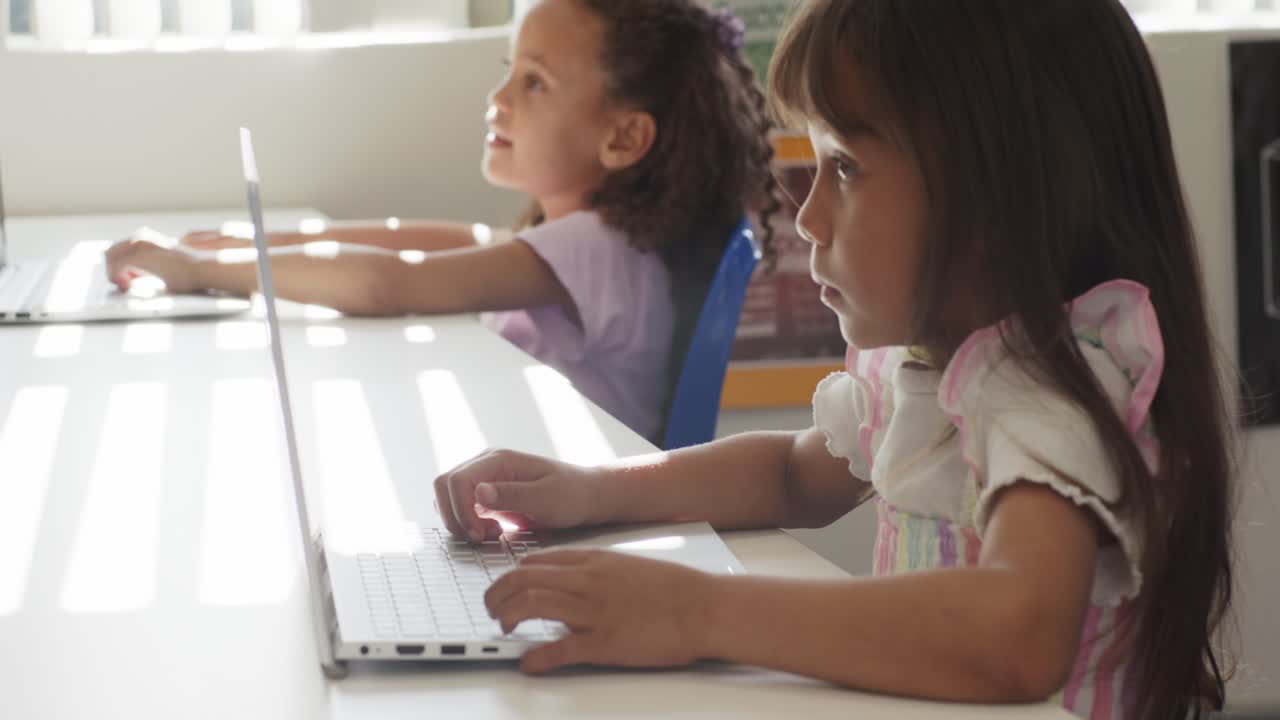Ragazze afroamericane in età scolare che digitano e si allungano, mentre la telecamera esegue una panoramica, lavorando sui loro laptop.