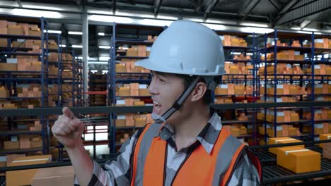 vista lateral de cerca de un ingeniero masculino asiático con casco de seguridad de pie en el almacén con estantes llenos de mercancías de entrega. estando enojado, señalándote y gritando en el almacenamiento