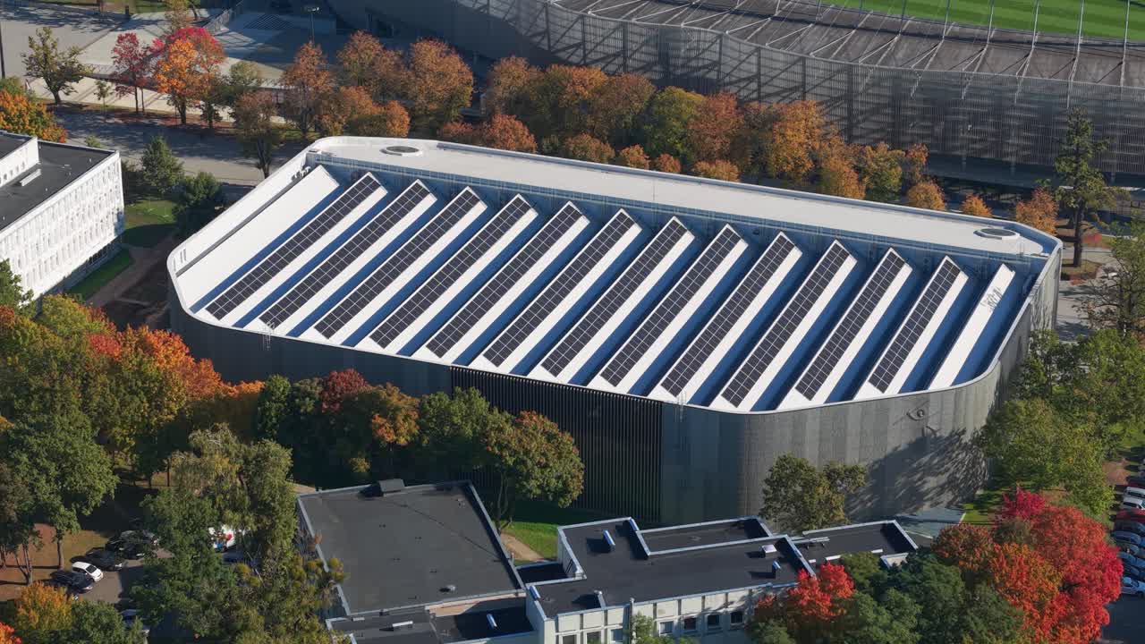 Modern building with solar panels on the rooftop surrounded by colorful autumn trees in Kaunas, Lithuania. Aerial view showcasing sustainable architecture and green energy solutions