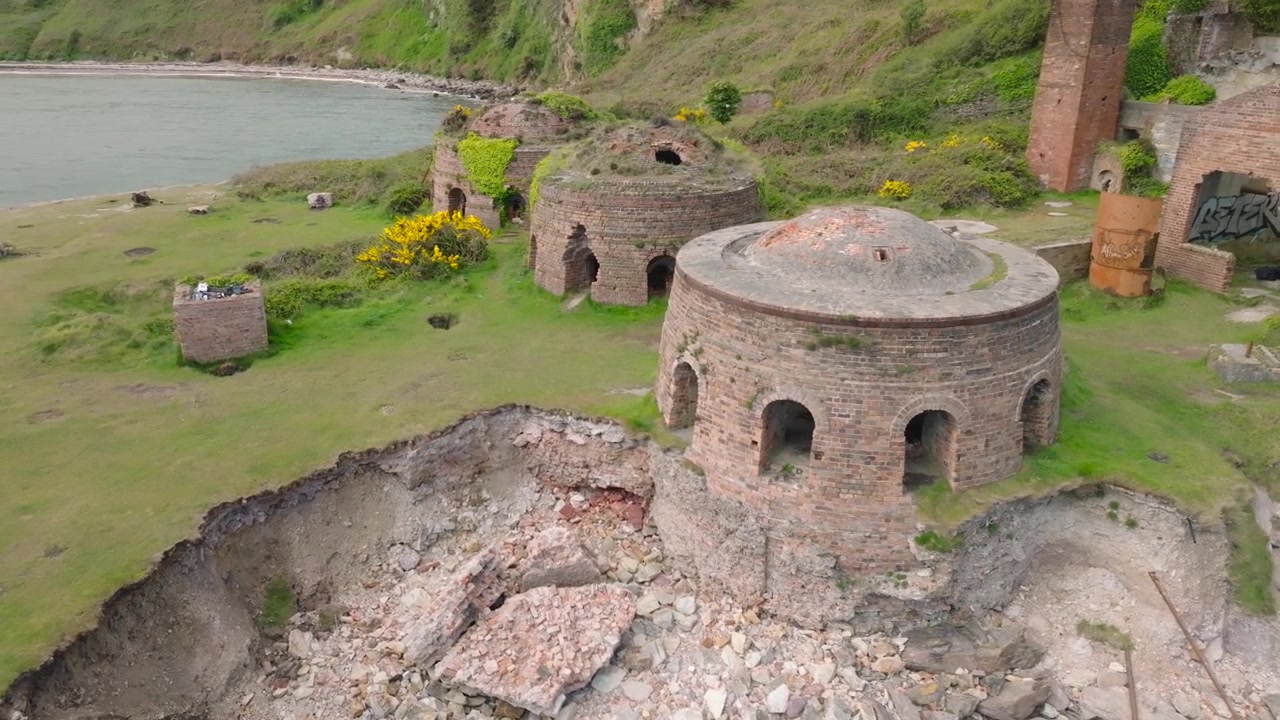 Porth Wen Brickworks, Anglesey, Wales. Långsam drönarorbit som visar övergivna bikupugnar med kust och hav synligt.