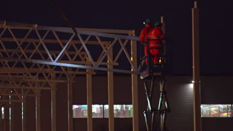 Worker-dressed-in-orange-overall,-on-a-crane-in-a-building-under-construction-at-the-night