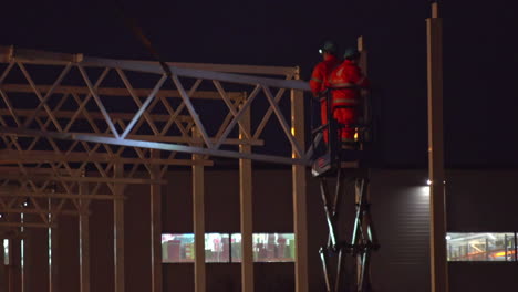 worker dressed in orange overall, on a crane in a building under construction at the night