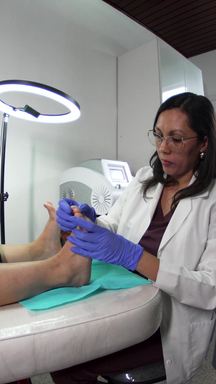 Female Podiatrist in White Coat and Blue Gloves Treating Patient Foot on Teal Drape in Professional Podology Clinic