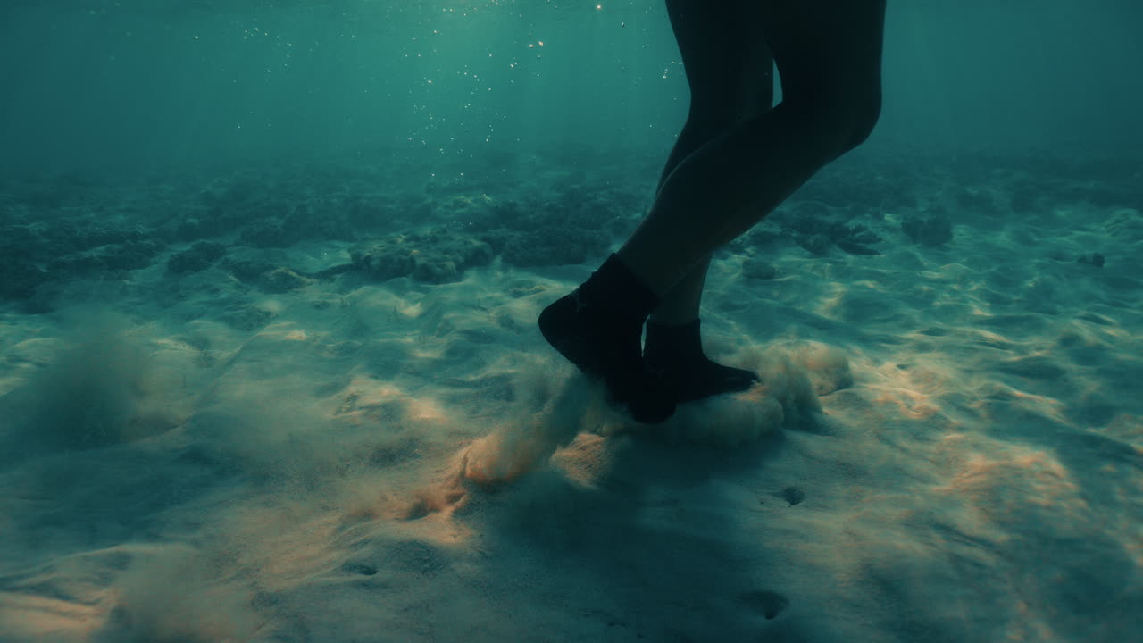 Freediver Walking Across Sandy Seabed, Underwater shot of a diver’s legs and fins stirring sand clouds as they walk across the seabed