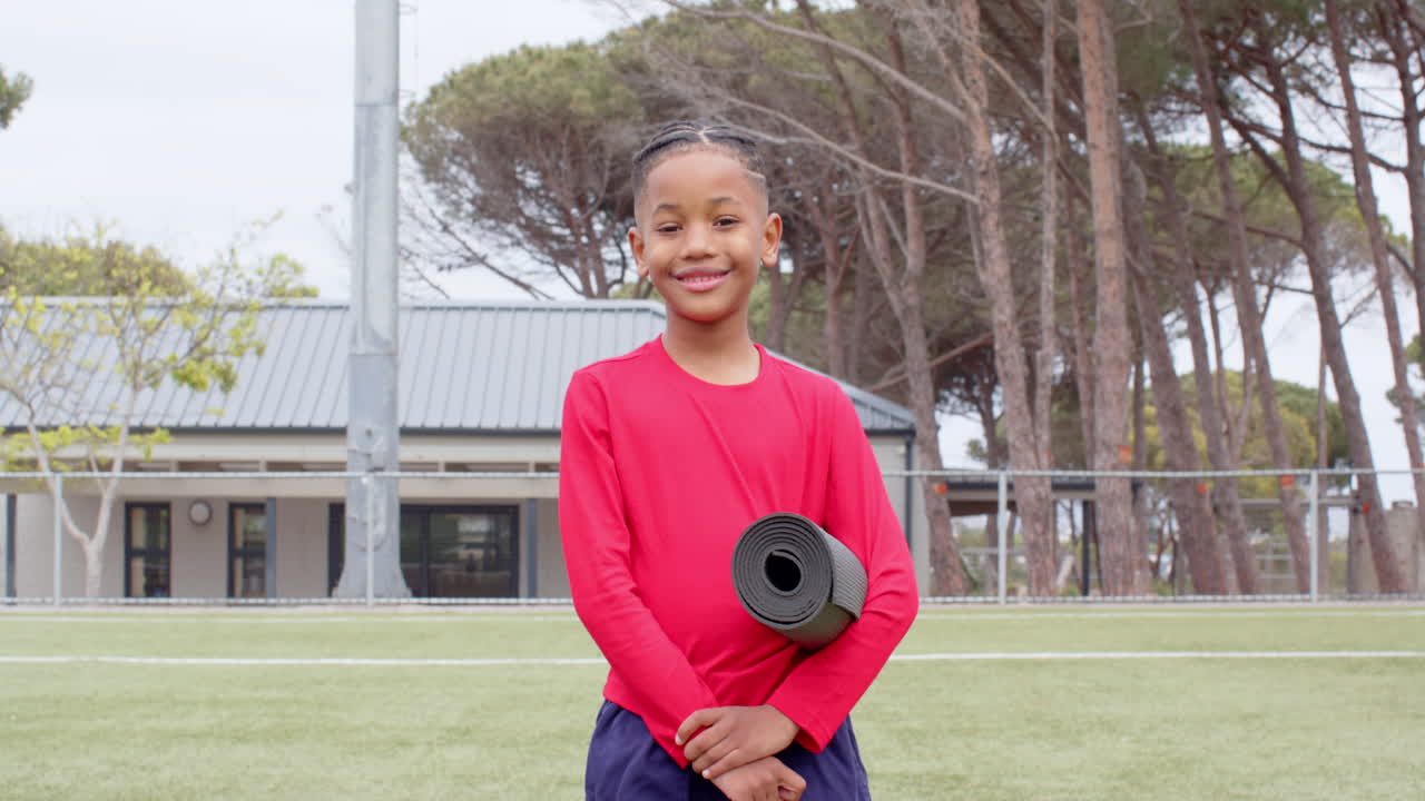 Smiling boy holding yoga mat on school field