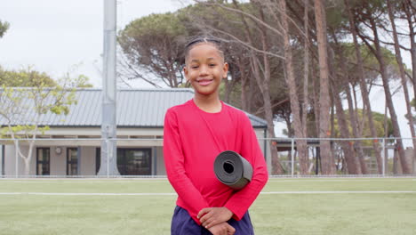 smiling boy holding yoga mat on school field