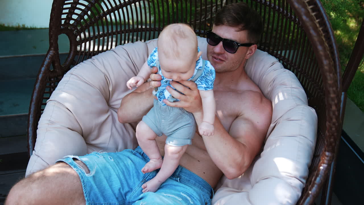 Dad and infant son sitting in the egg chair. Loving father kisses his baby on the back. Top view.