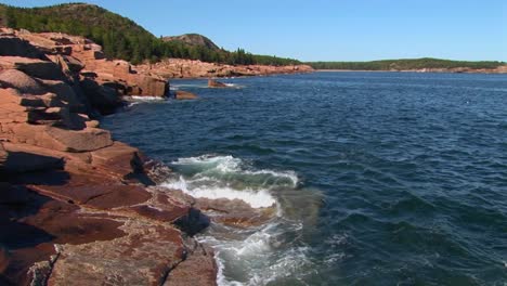 water crashes against rocks that are near trees and a mountain range in acadia national park in maine