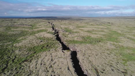 aerial view of a large crack in the ground between two tectonic plates in a volcanic rift zone in iceland. the landscape shows the distinct separation of the plates and the rugged terrain.