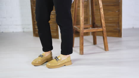 female walking back and forth in fashionable new shoes. beige stylish footwear on plain soles with chain decoration. wooden stool and folding screen at backdrop.