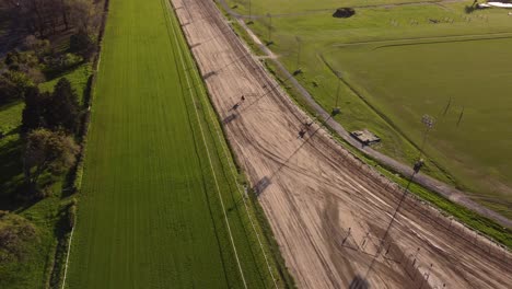 Toma-Aérea-De-Dos-Caballos-De-Carrera-Caminando-En-La-Pista-De-Carreras-De-Arena-Durante-La-Sesión-De-Entrenamiento-Para-La-Carrera