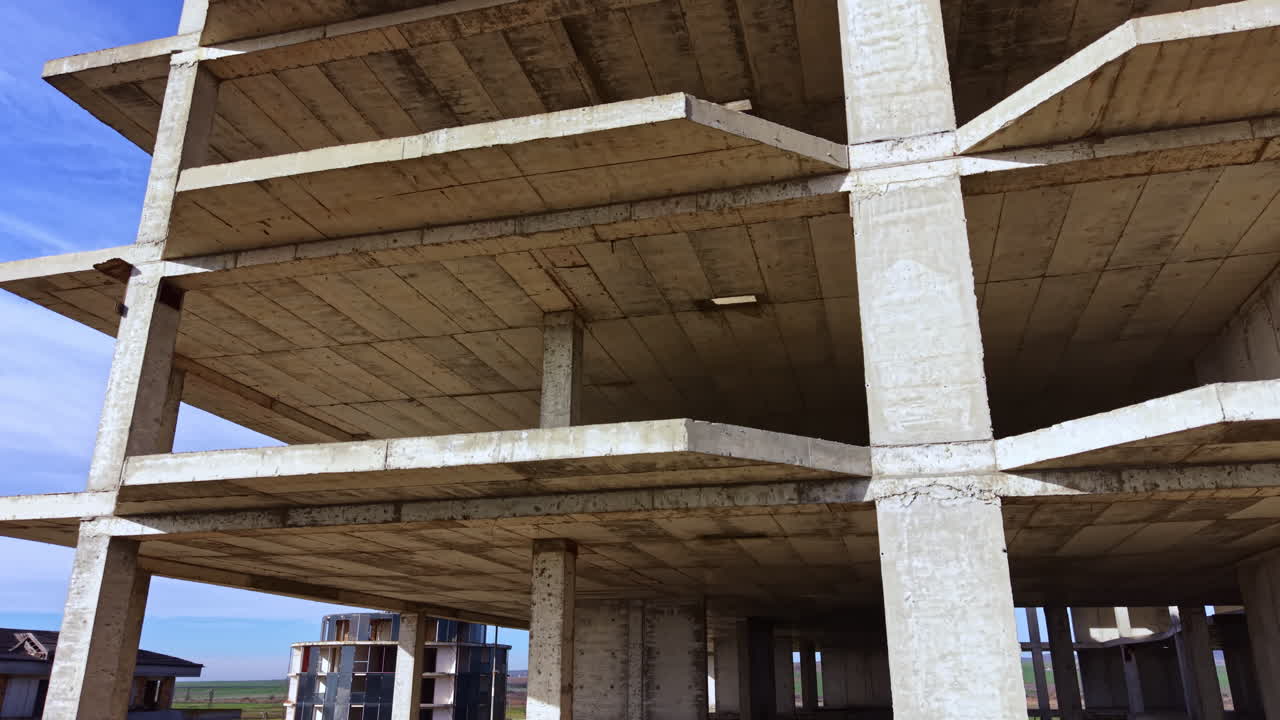 Concrete structure reaches for the sky with empty spaces revealing raw power in a bold, unfinished design under a bright blue sky