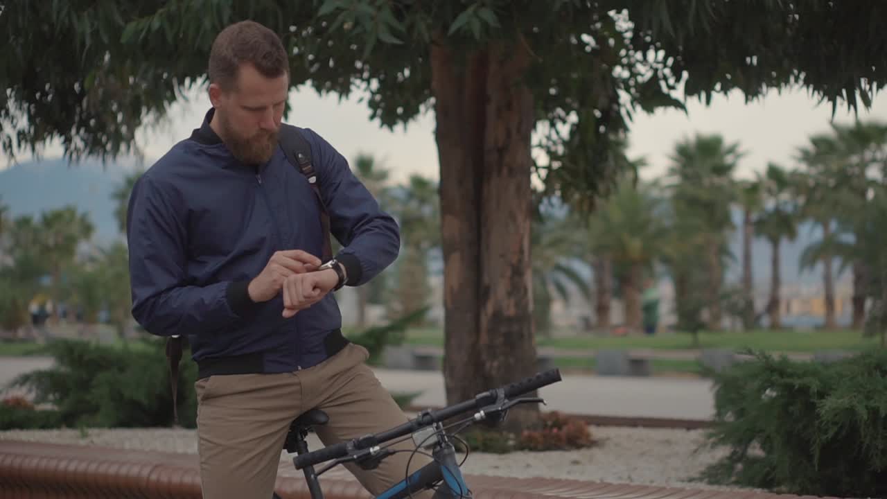Man Checking Time on Smartwatch Beside Bicycle in Park