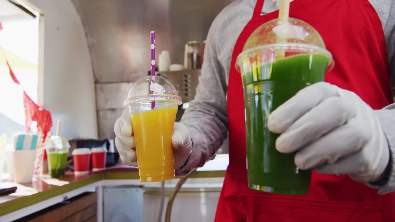 Seção central de homem afro-americano usando avental servindo smoothies para um casal em food truck