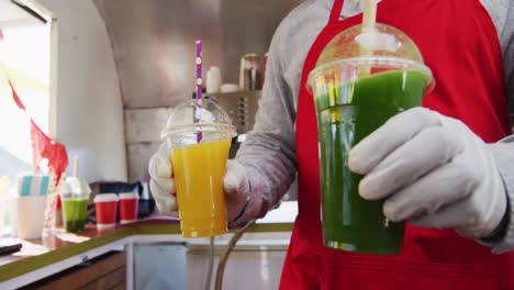 mid section of african american man wearing apron serving smoothies to a couple at the food truck